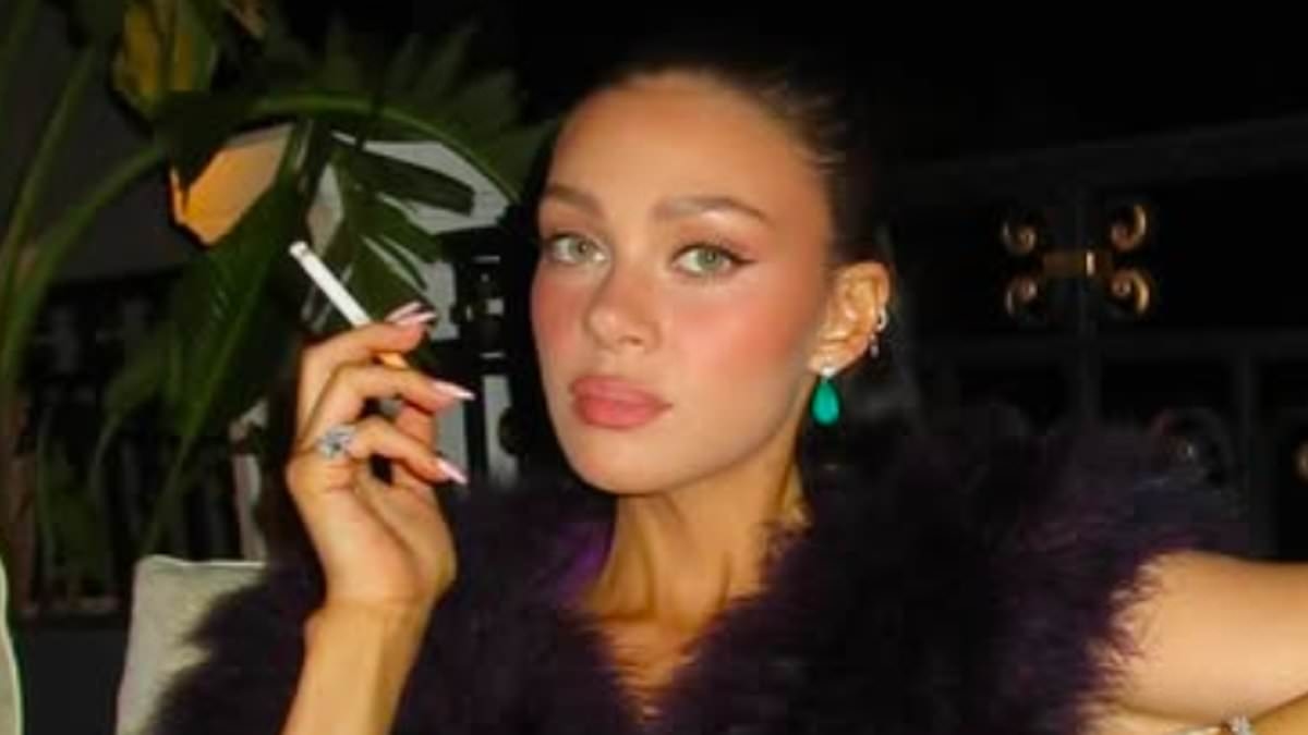Nicola Peltz shares yet another sultry snap as she puffs on a cigarette and poses in a skimpy purple crop top - after sharing naked bath picture