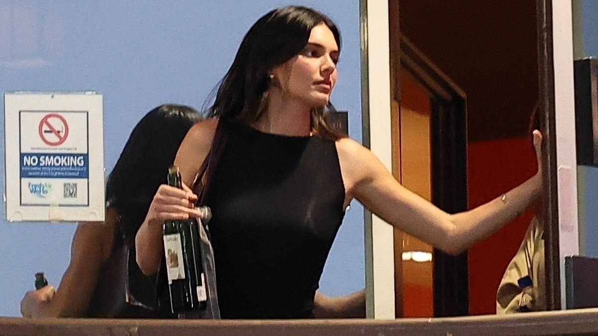 Kendall Jenner cuts a chic figure in a black jumpsuit and clutches a bottle of wine after enjoying dinner with friends